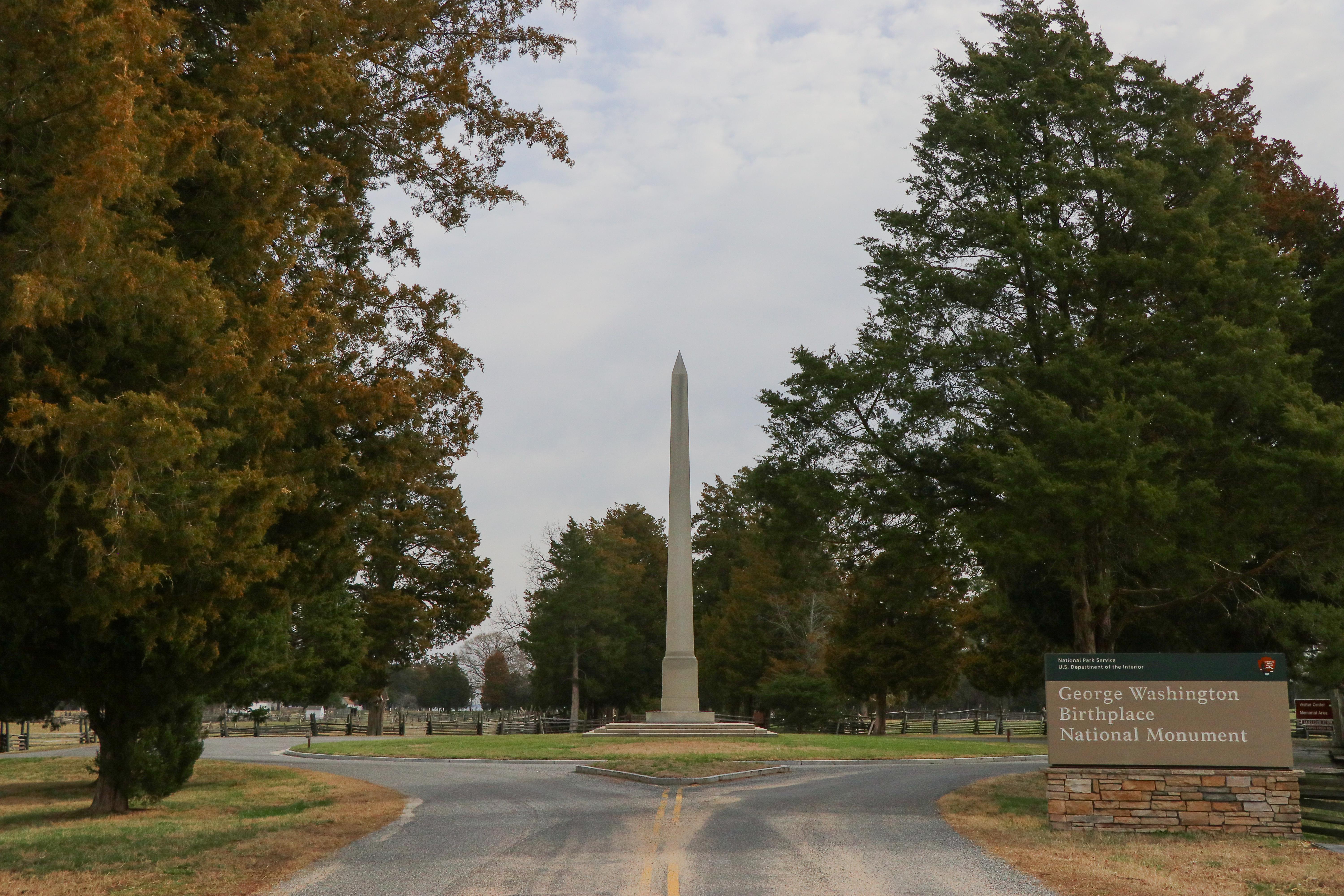 White obelisk in a roundabout, surrounded by trees and the park sign