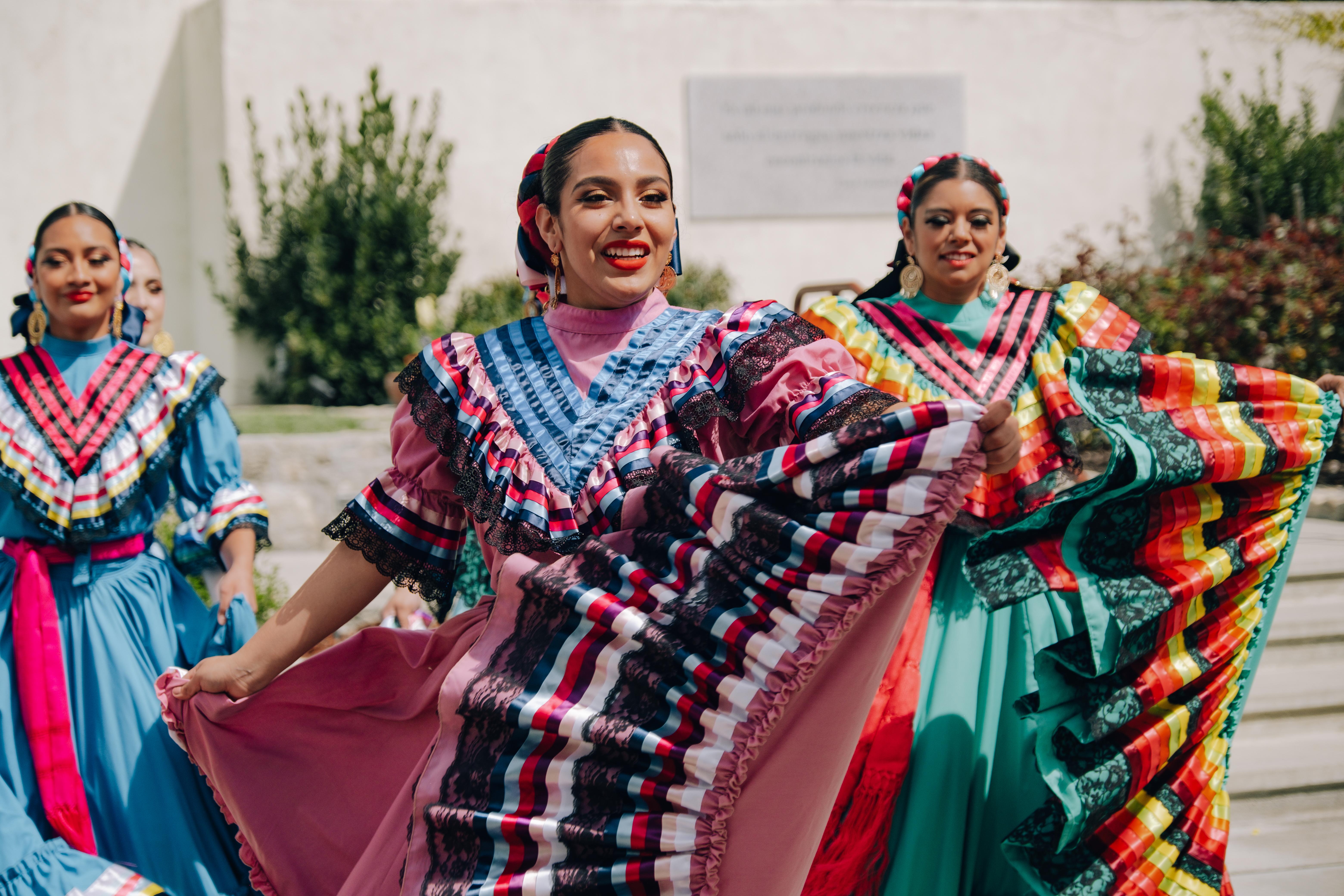 A set of folklorico dancers in traditional regalia dance together.