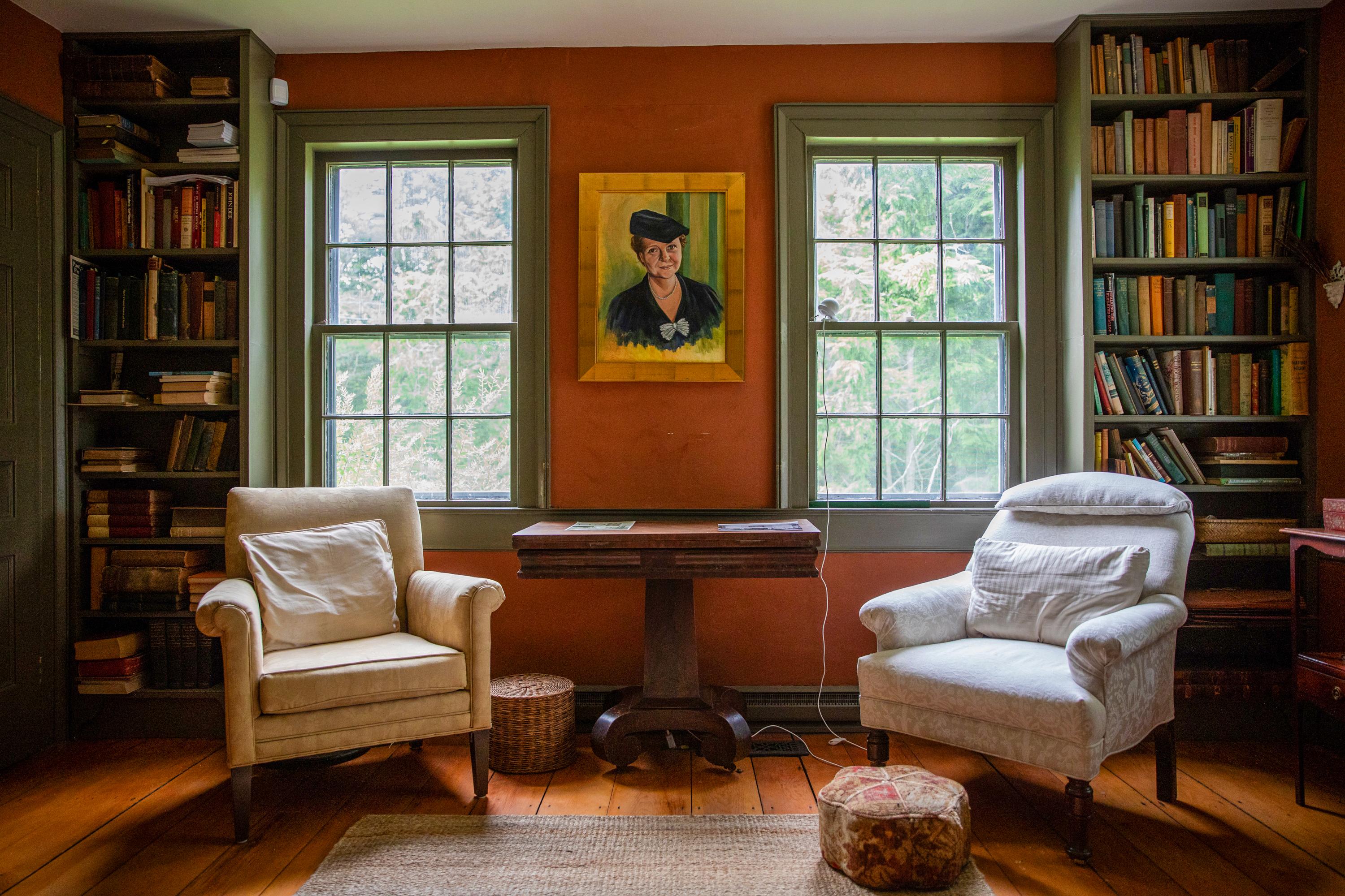 Two white sofa chairs stand in front of two windows in a room with red walls and a portait of Perkin