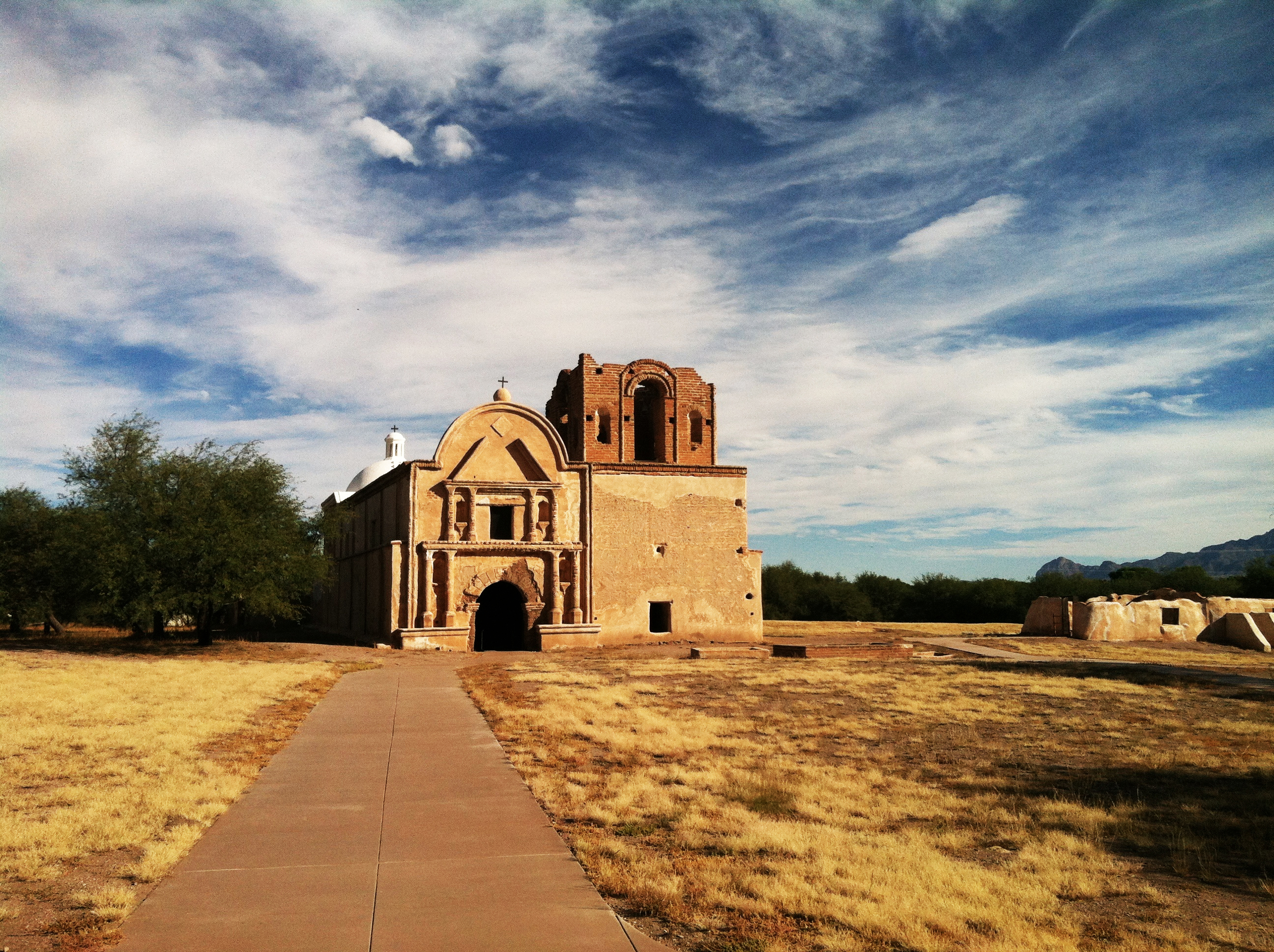 long paved sidewalk leads to adobe mission church