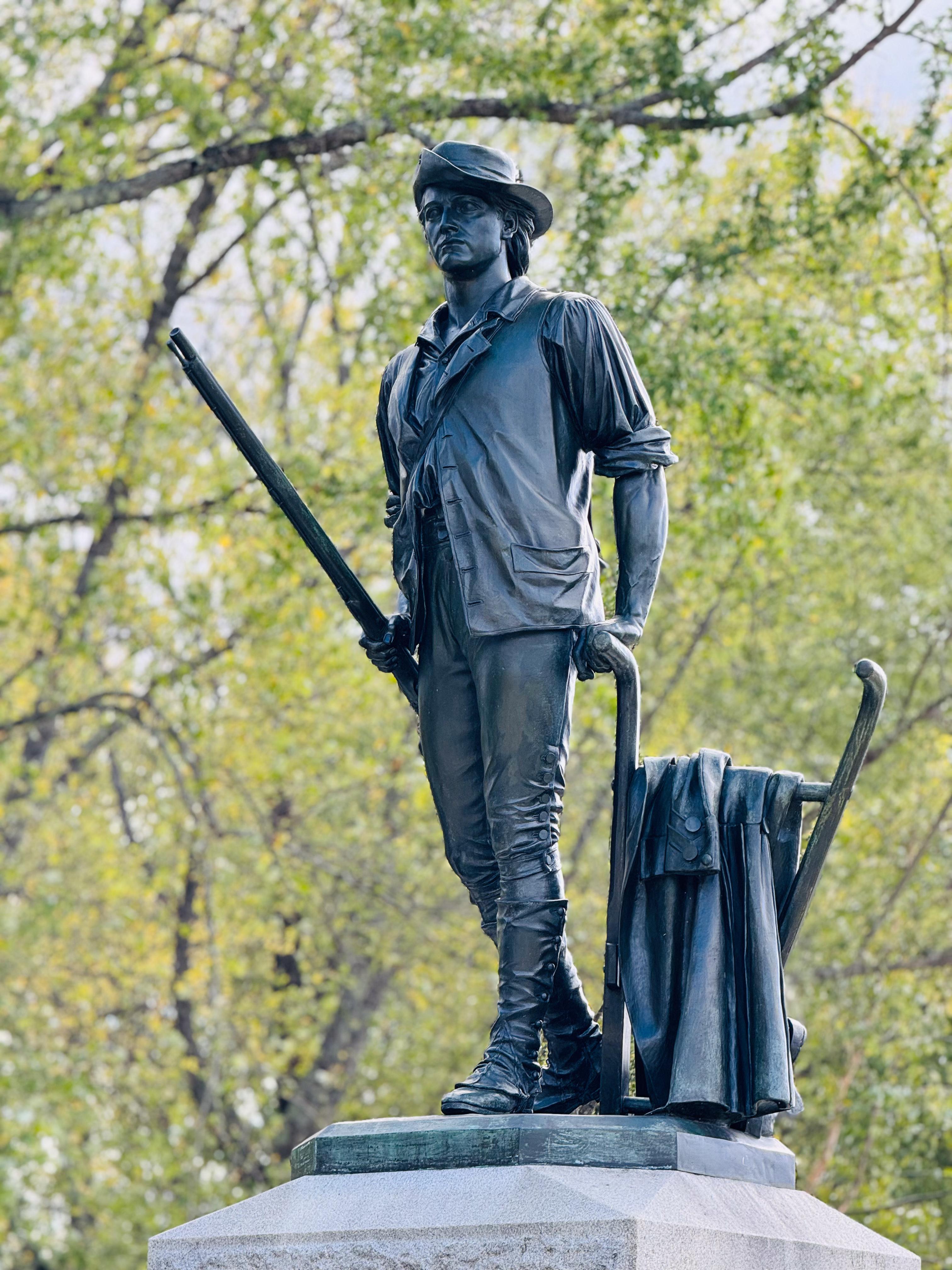 A bronze statue of a minute man stands with musket and plow