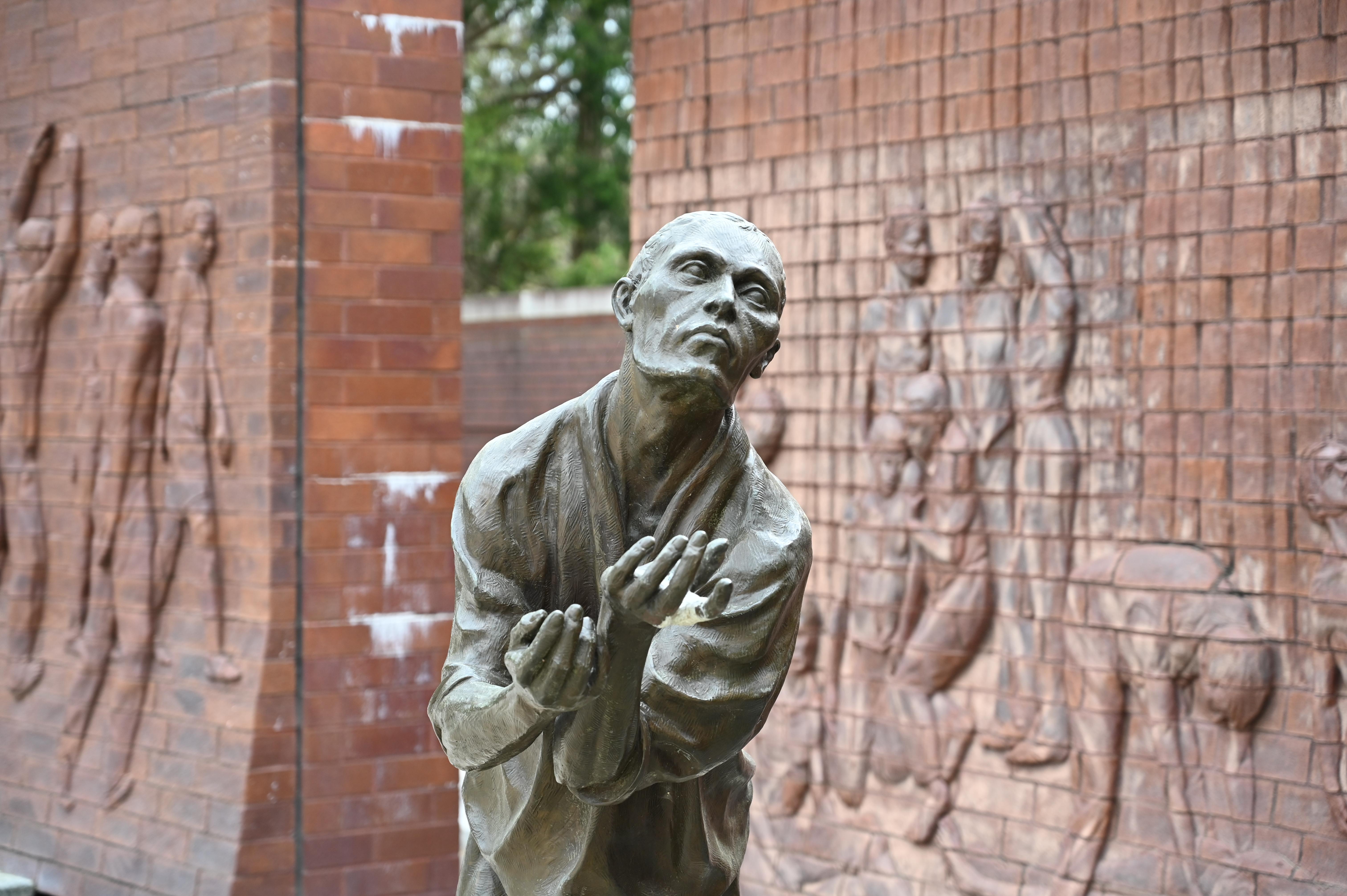 stone statue stands with his arms stretched forward. Two large stone walls sit behind him.