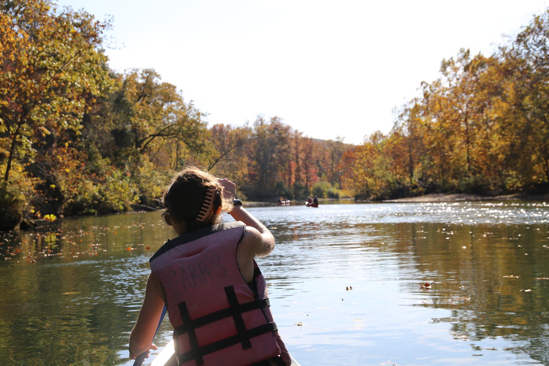 A woman paddles down a river while wearing a personal flotation device.