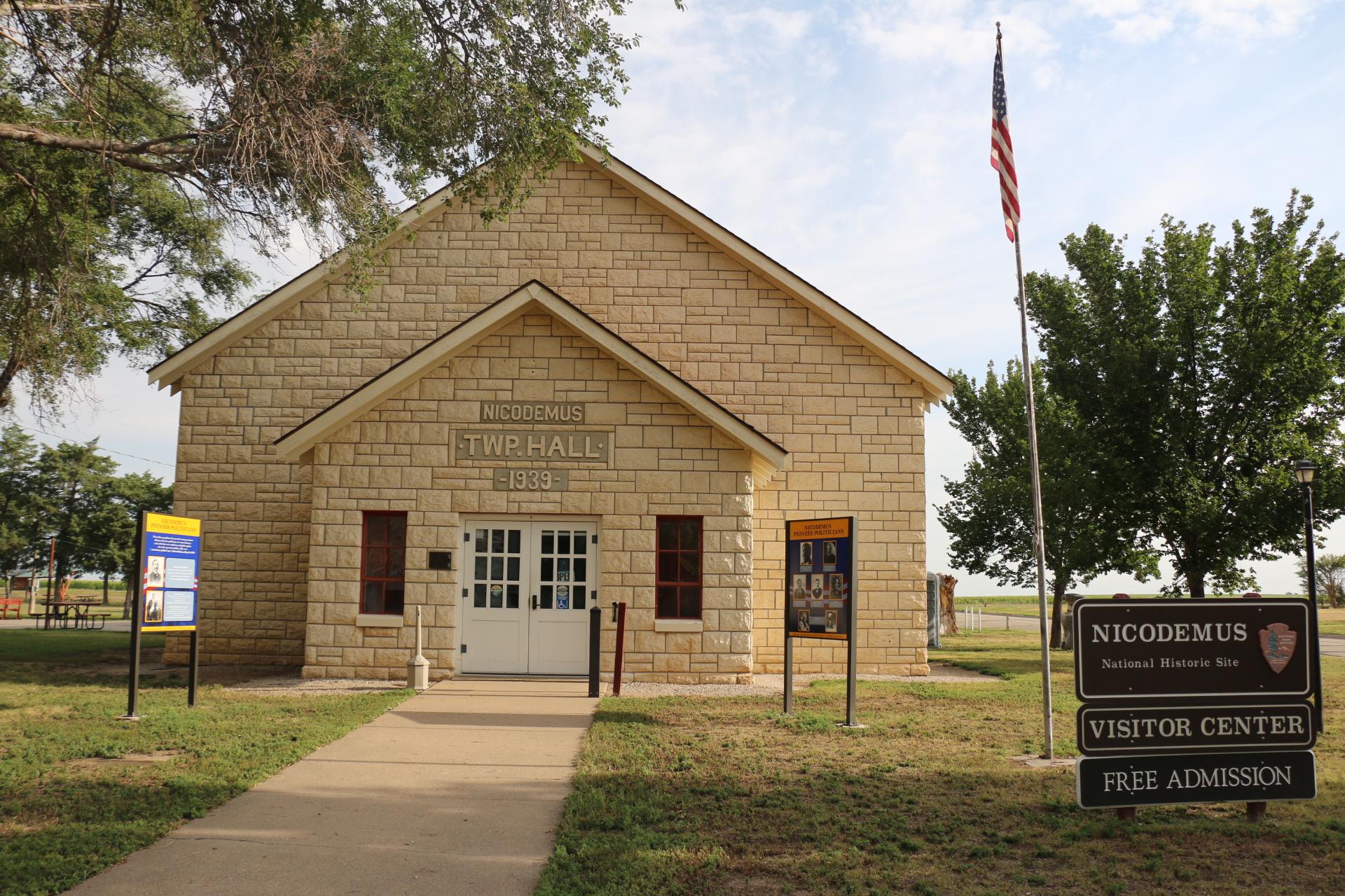 Front view of limestone building. A sidewalk leads up to white double doors of the building.