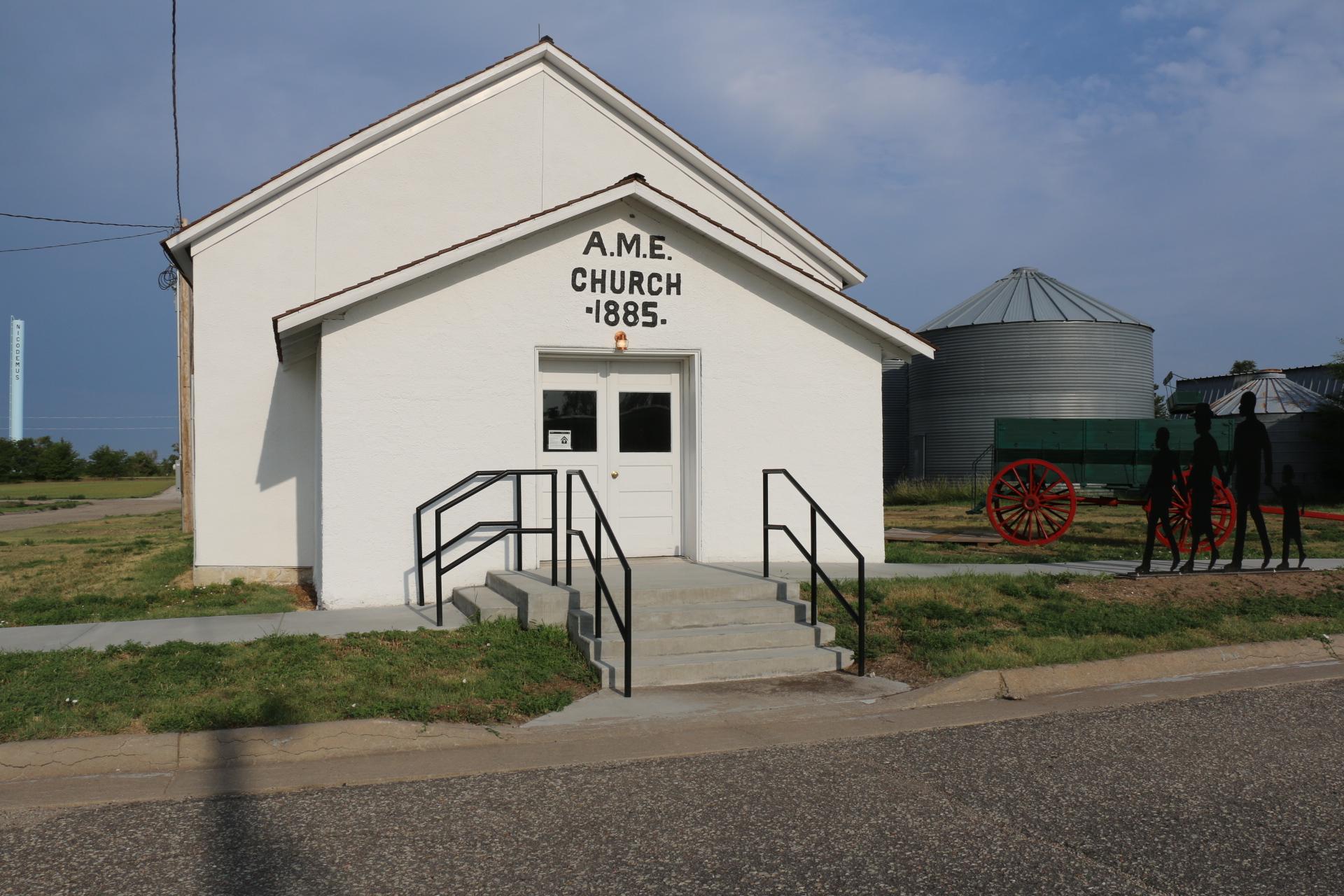 White stucco church with white double doors and text above the doors that reads "A.M.E. CHURCH 1885"